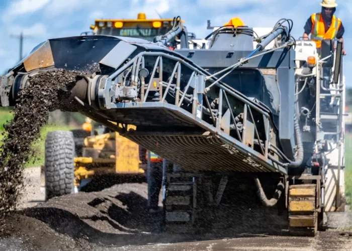 A machine from The Miller Group pours recycled material onto a roadway. 