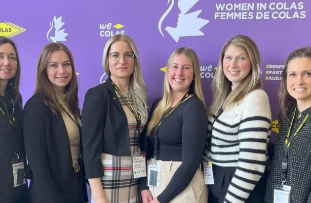 Five women posing for a photo in front of the Women in Colas Conference banner