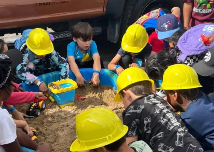 Children wearing construction hats play in a sandbox during The Miller Group's touch-a-truck event.