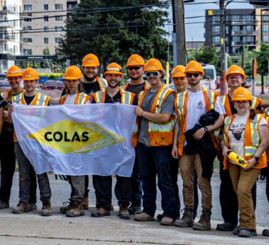 Group of students wearing construction gear holding a Colas flag