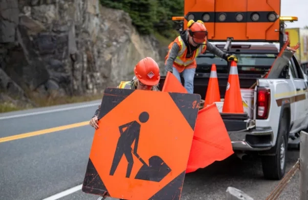 Who workers placing a road construction safety sign on the road