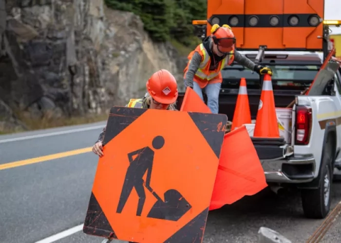 Who workers placing a road construction safety sign on the road
