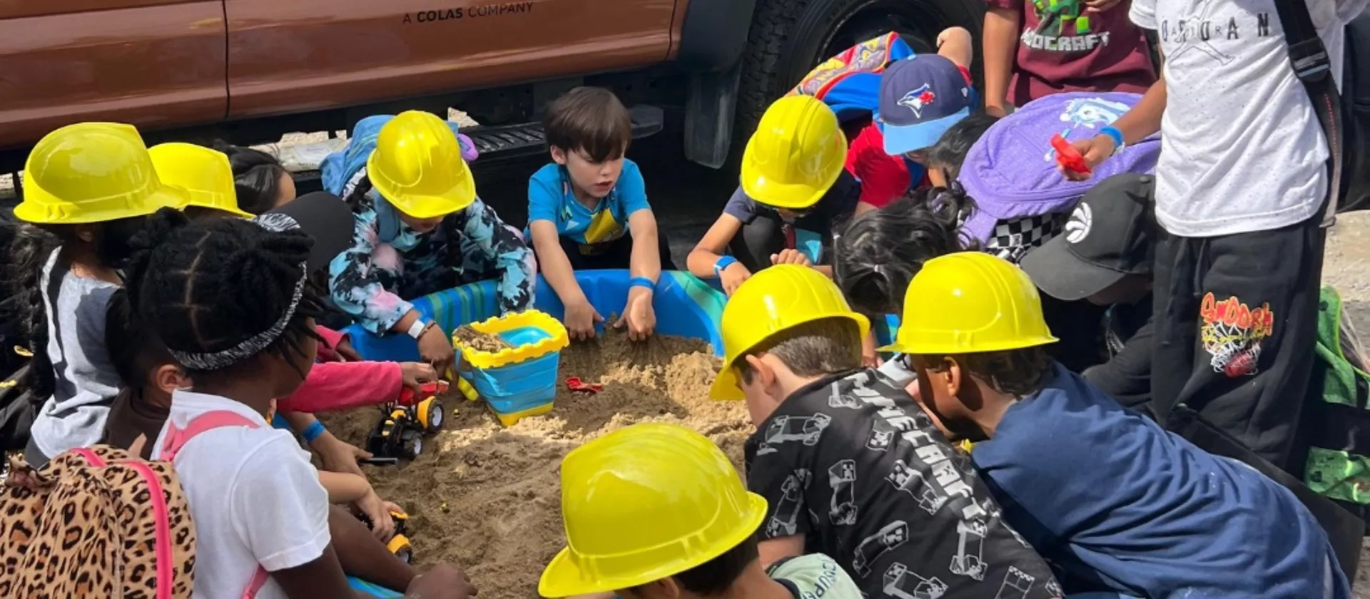 Children wearing construction hats play in a sandbox during The Miller Group's touch-a-truck event.
