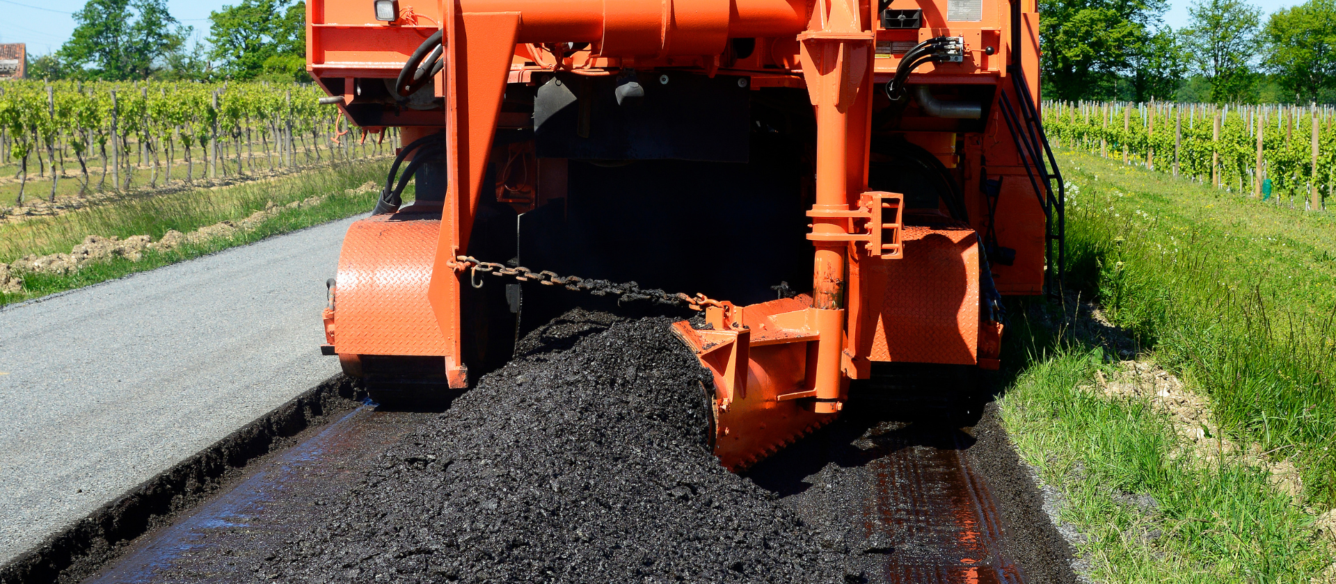 A machine lays down a layer of fresh asphalt onto a road.