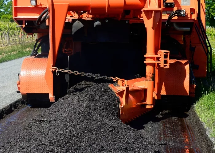 A machine lays down a layer of fresh asphalt onto a road.
