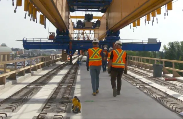 Crews on the Edmonton LRT walk under the gantry crane construcing the elevated portion of the tracks.